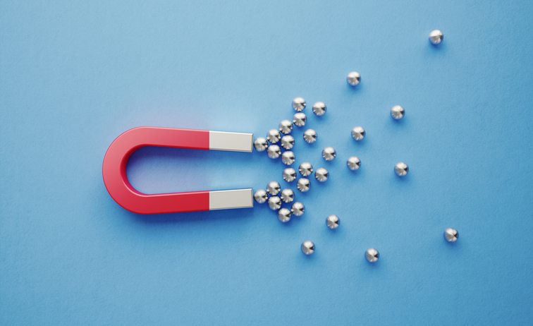Red horseshoe magnet attracting metallic balls on a blue background – concept of Magnetic Activated Cell Sorting (MACS) in fertility treatment.