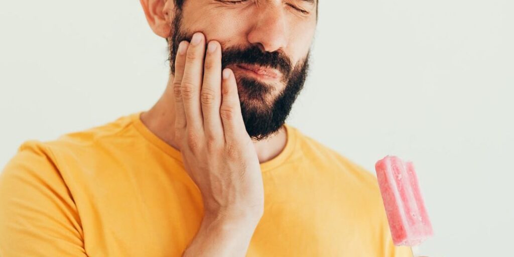 Person feeling sharp tooth pain while drinking cold water due to tooth sensitivity